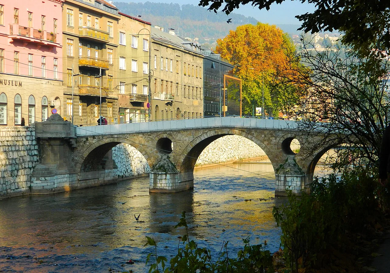 Latin bridge (prev. Princip bridge) in Sarajevo. Across the bridge is a street of several grayish houses not more than four stories high.