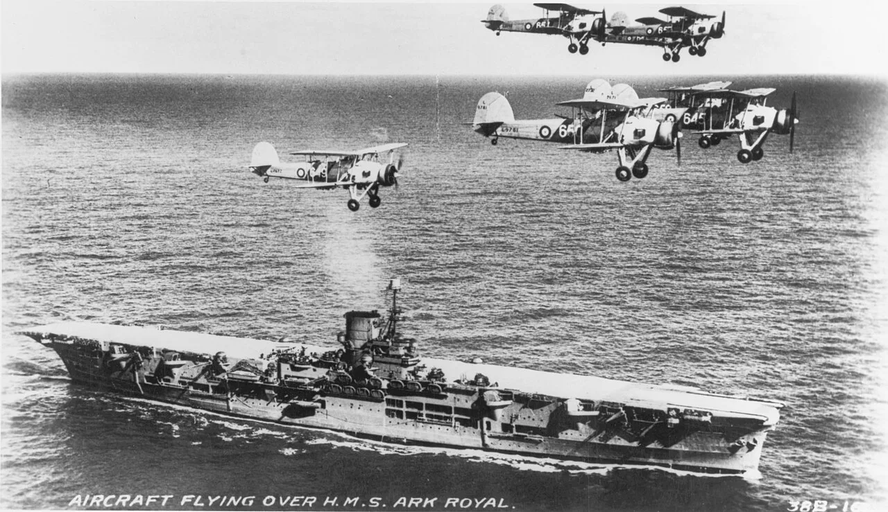 The aircraft carrier HMS Ark Royal with a flight of Swordfish overhead