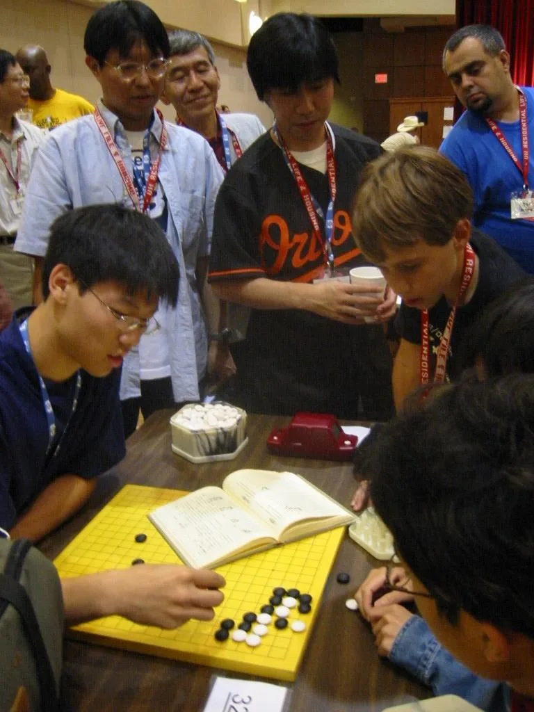 Three Japanese professional Go players observe some younger amateurs as they dissect a life and death problem in the cor