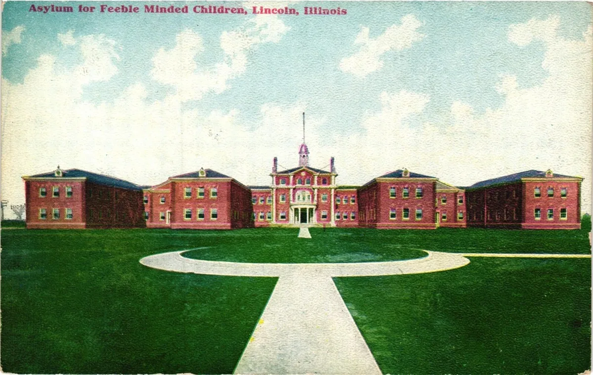 A colored postcard showing a large complex of brick buildings behind a large grassy pavilion