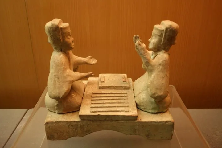 Eastern Han glazed pottery tomb figurines playing Liubo, with six sticks laid out to the side of the game board