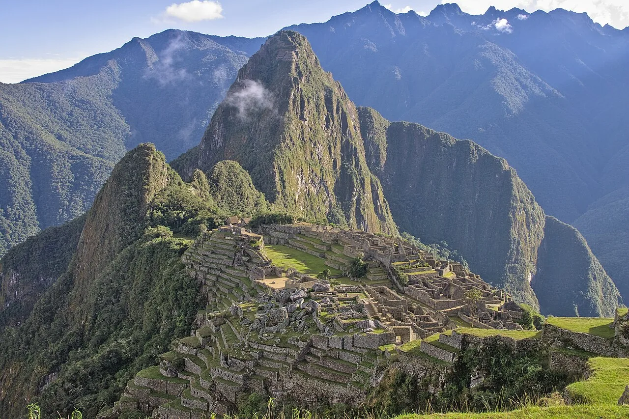 Stone ruins of Machu Picchu set on a mountain ridge, with steep green peaks in the background.